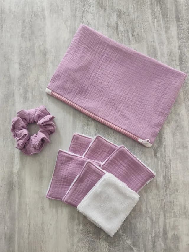 Pochette zippée mauve accompagnée d'un chouchou et de lingettes lavables assorties sur fond gris.