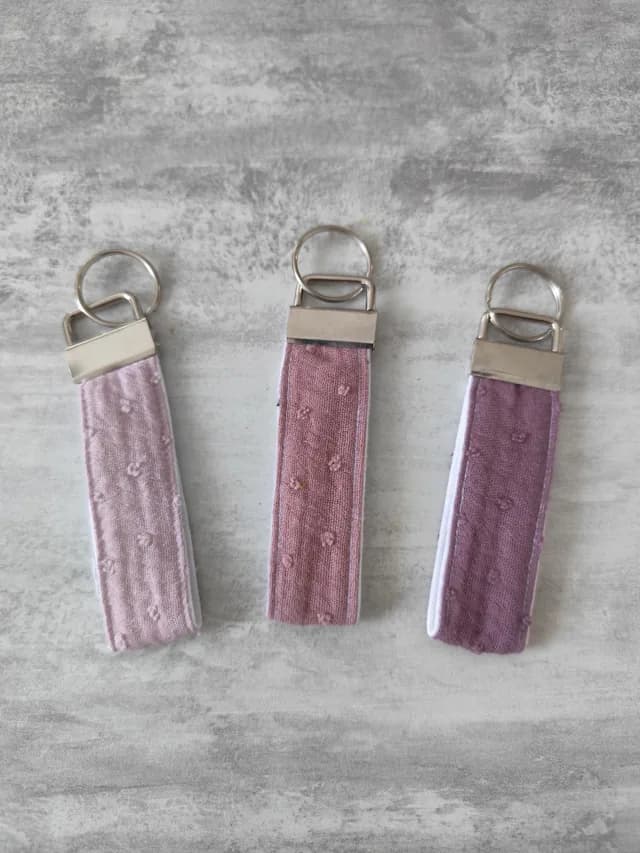 Trois porte-clés lanières en tissu rose pâle, rose poudré et violet avec embouts métalliques