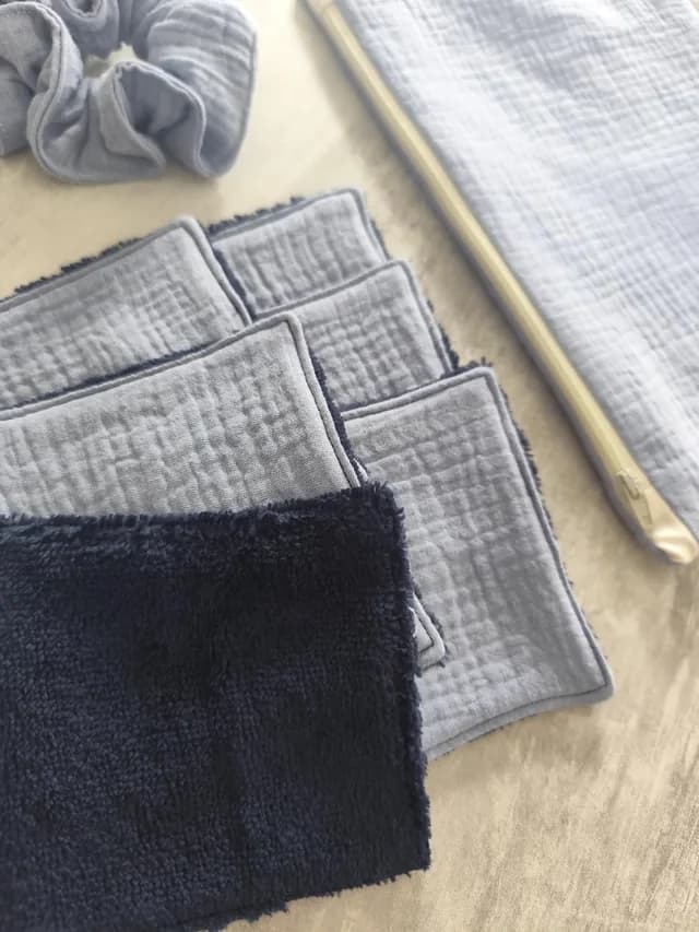 Gros plan sur les lingettes lavables en tissu bleu texturé et éponge sombre, avec chouchou et pochette.