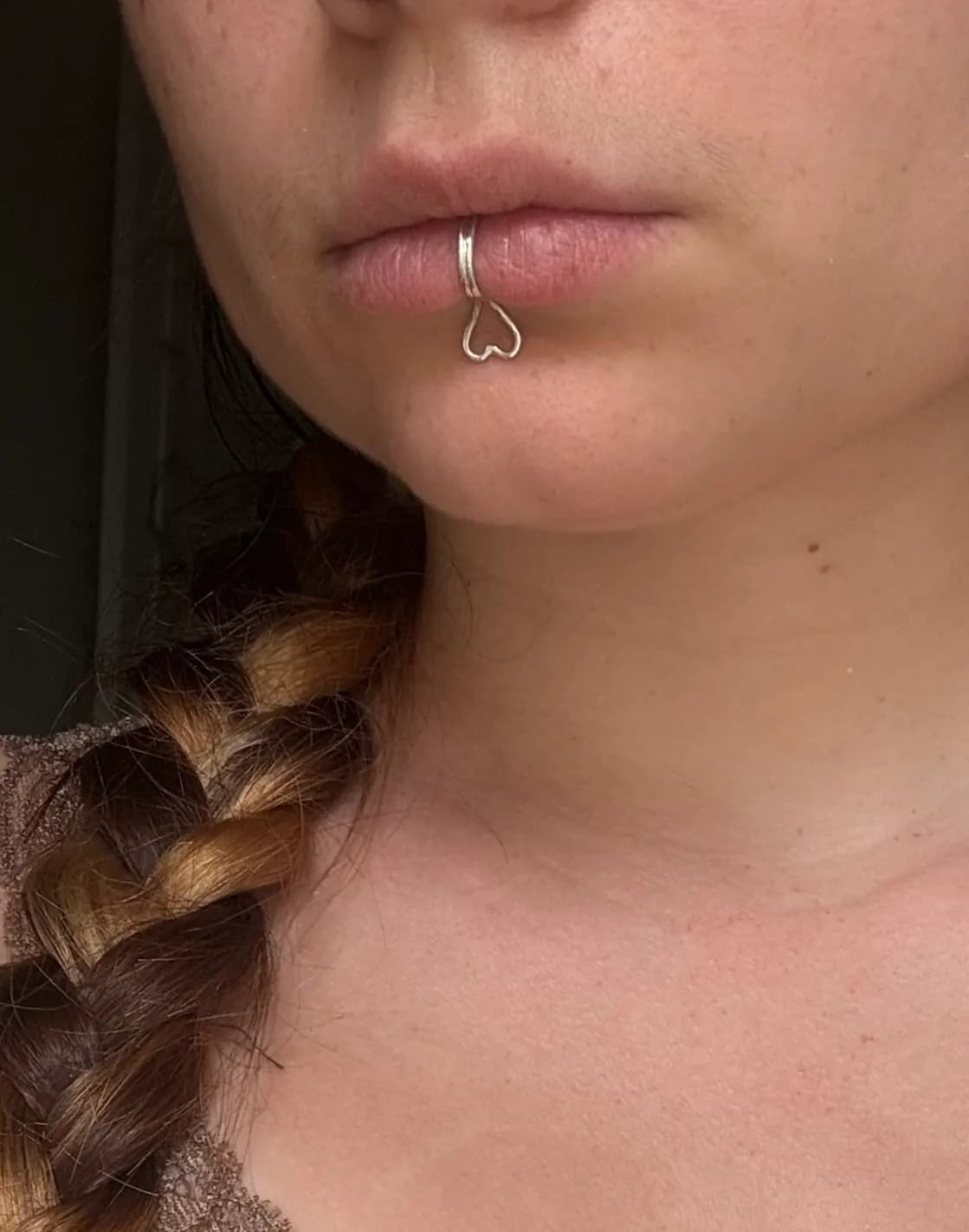 Bague de lèvre en argent avec motif cœur ajouré, portée sur la lèvre inférieure, vue de trois-quarts.