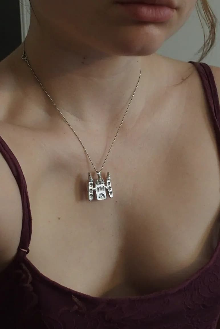 Pendentif en étain en forme de château avec tours porté autour du cou sur une fine chaîne.