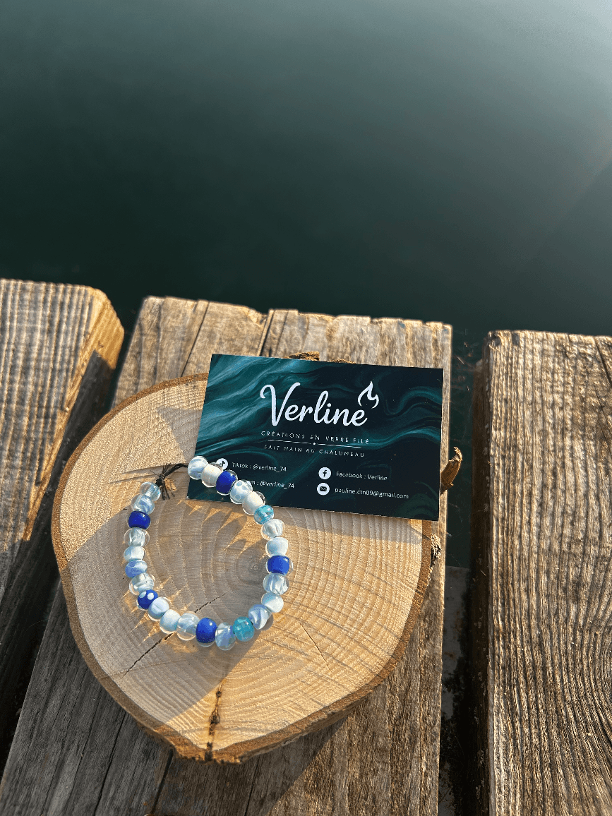 Bracelet en perles de verre bleues et marbrées posé sur une rondelle de bois brut à côté d'une carte