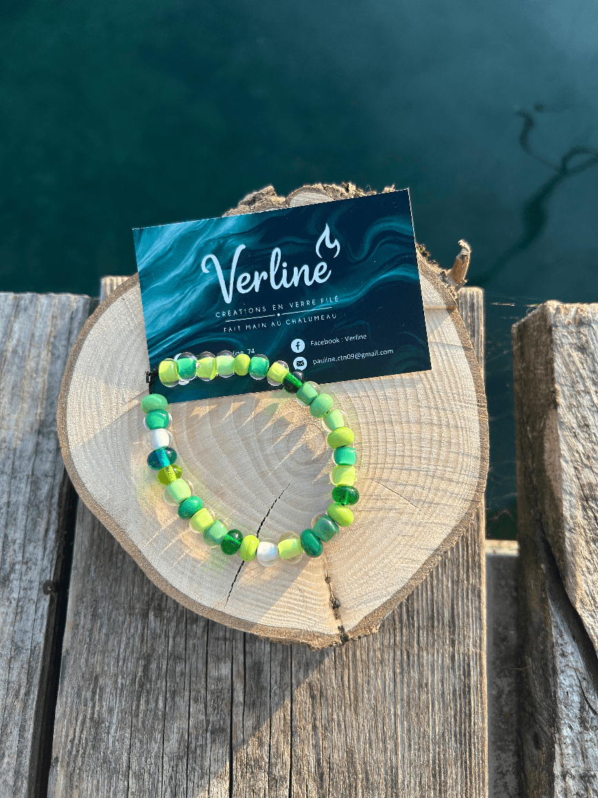 Bracelet artisanal aux perles rondes dans les nuances de vert posé sur une tranche de bois