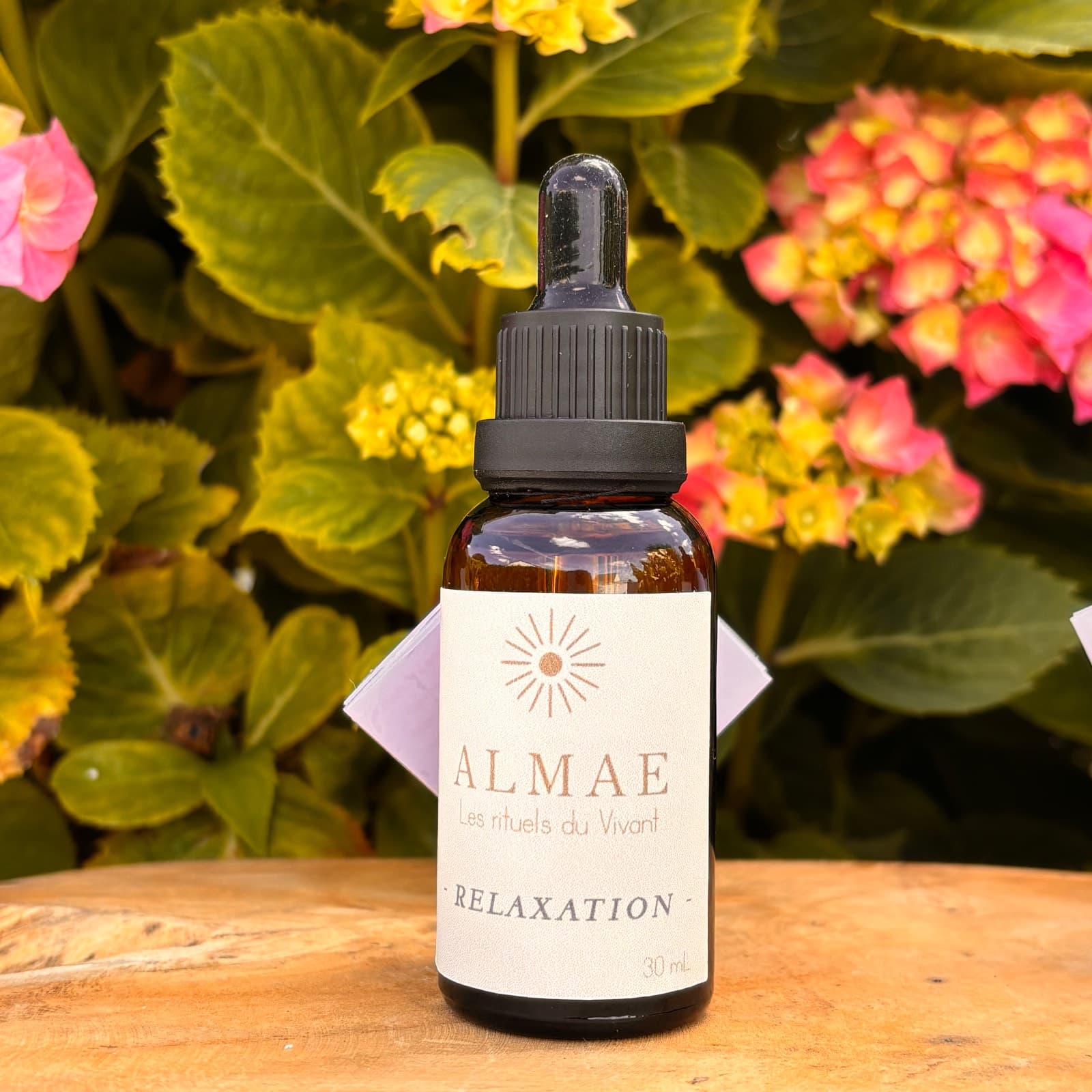 Flacon compte-gouttes en verre ambré de fondant liquide 30 ml Relaxation posé devant des fleurs.