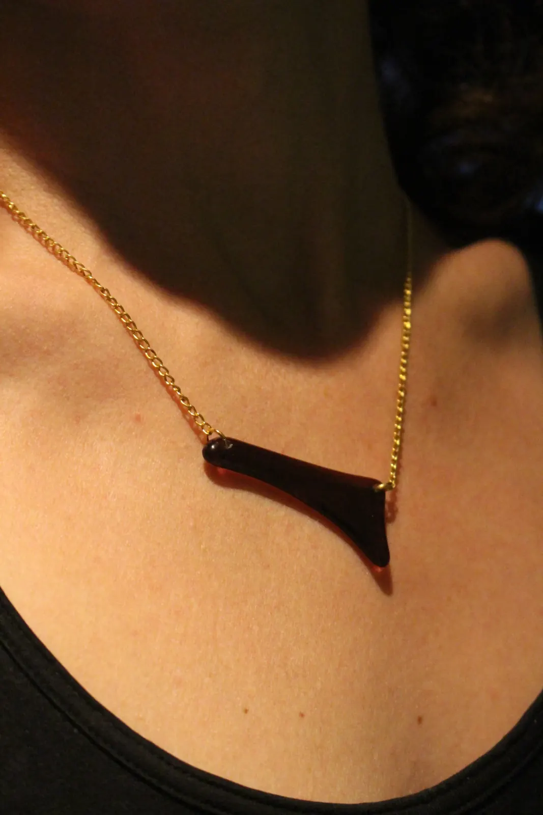 Collier avec pendentif asymétrique en verre sombre et chaîne dorée, porté au cou.