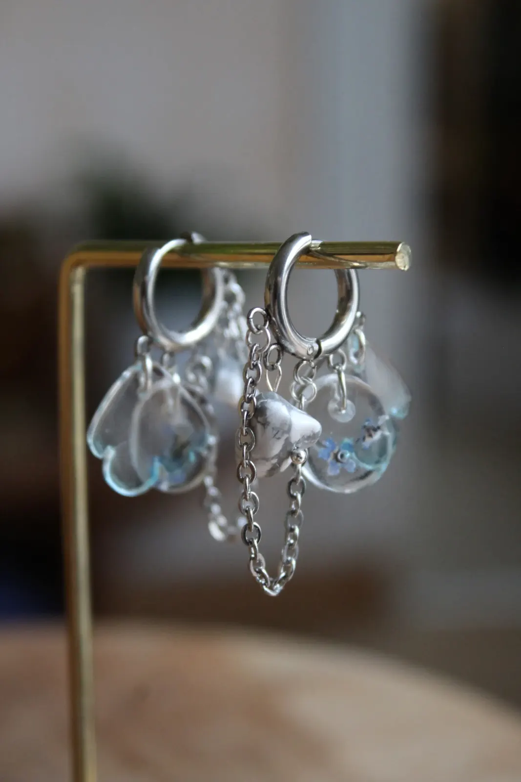 Paire de boucles d'oreilles créoles argentées suspendues côte à côte sur un présentoir doré.