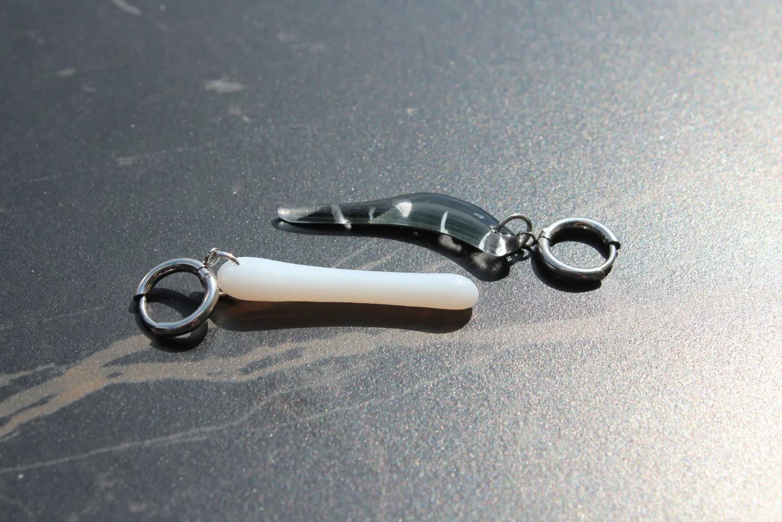 Paire de boucles d'oreilles asymétriques en verre noir et blanc posées à plat sur un fond sombre.