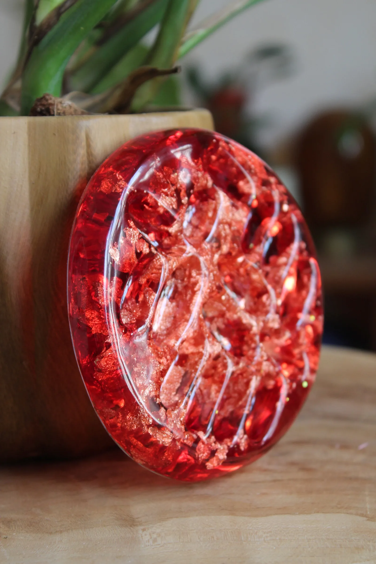 Coupelle en résine rouge translucide avec inclusions dorées scintillantes, appuyée contre un pot.