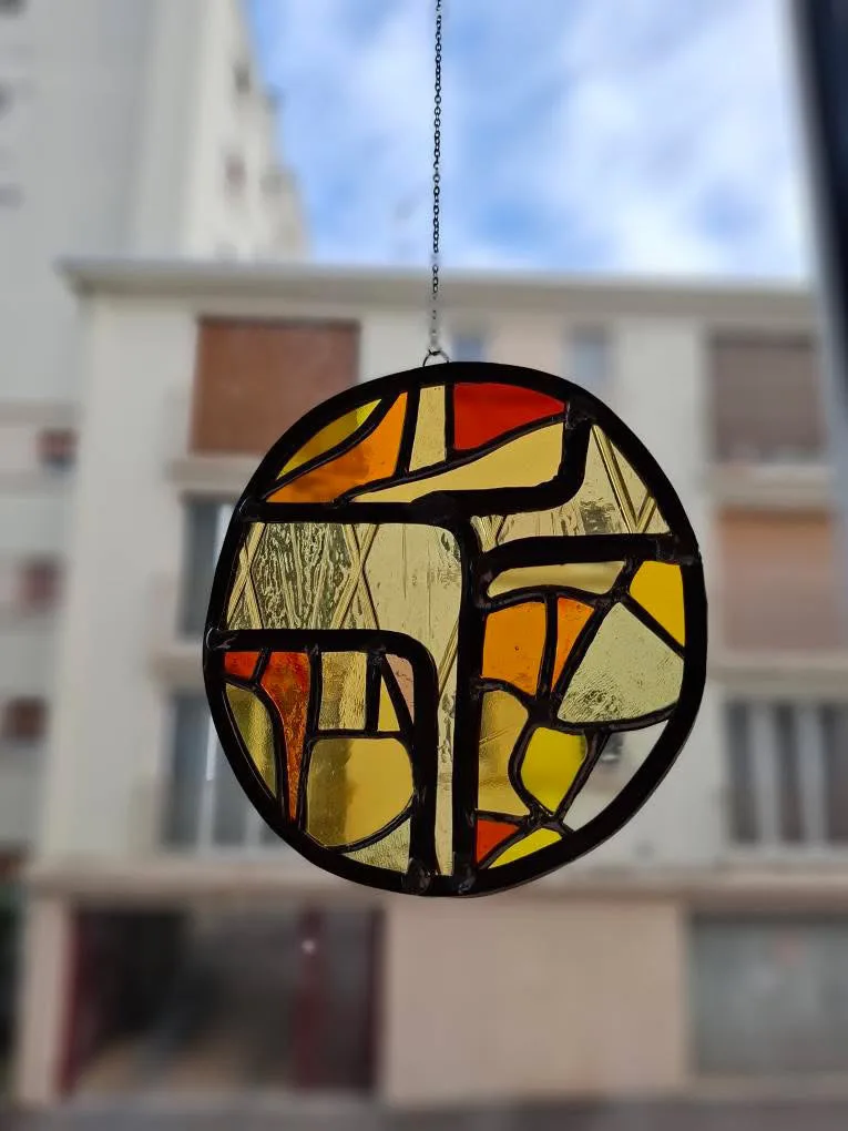 Gros plan sur un médaillon rond en vitrail aux motifs géométriques et abstraits jaune, ambre et rouge.