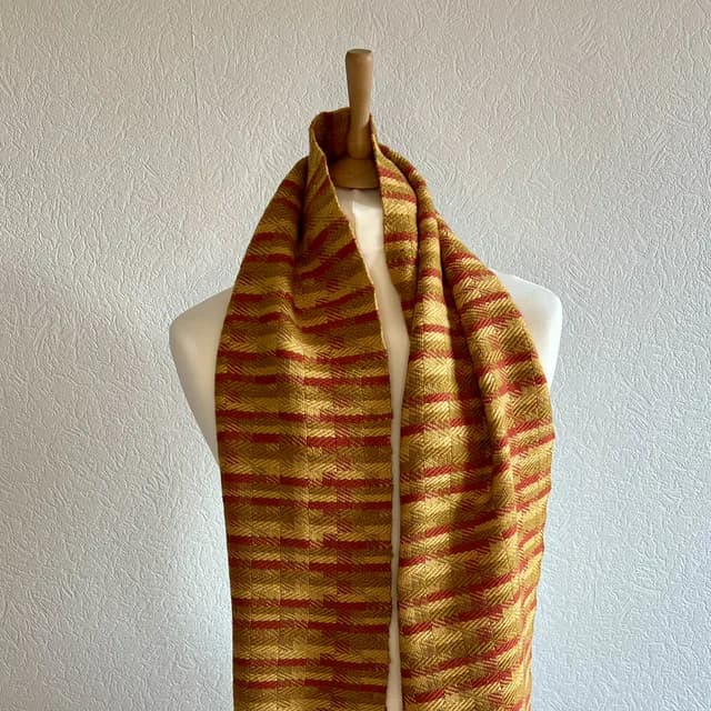 Écharpe tissée aux tons or et orange drapée sur un buste de mannequin