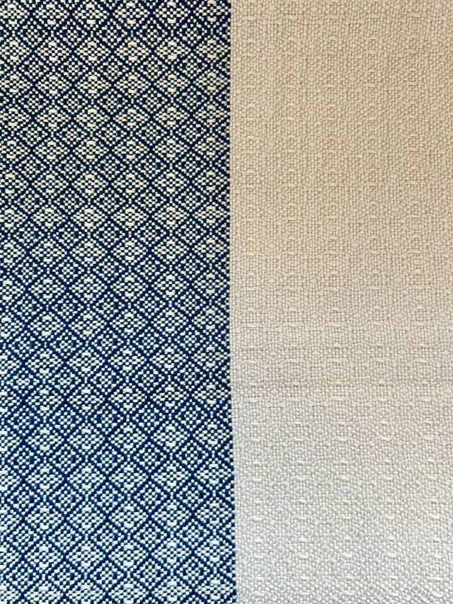 Gros plan sur le tissage bicolore d'une écharpe, motifs géométriques bleus et texture beige.