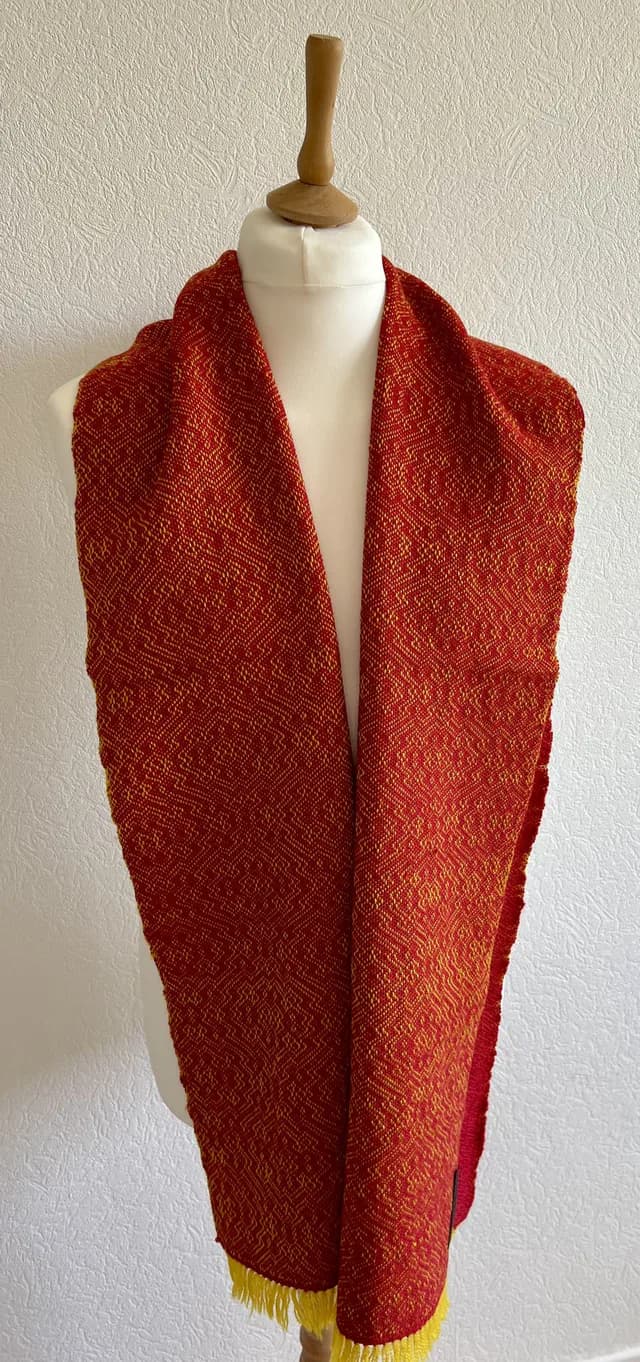 Écharpe tissée en laine rouge et jaune à motifs géométriques, présentée sur un mannequin de couture.