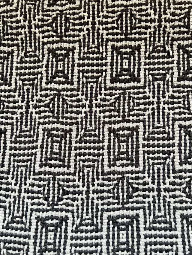 Gros plan sur le tissage artisanal aux motifs géométriques noirs et gris.