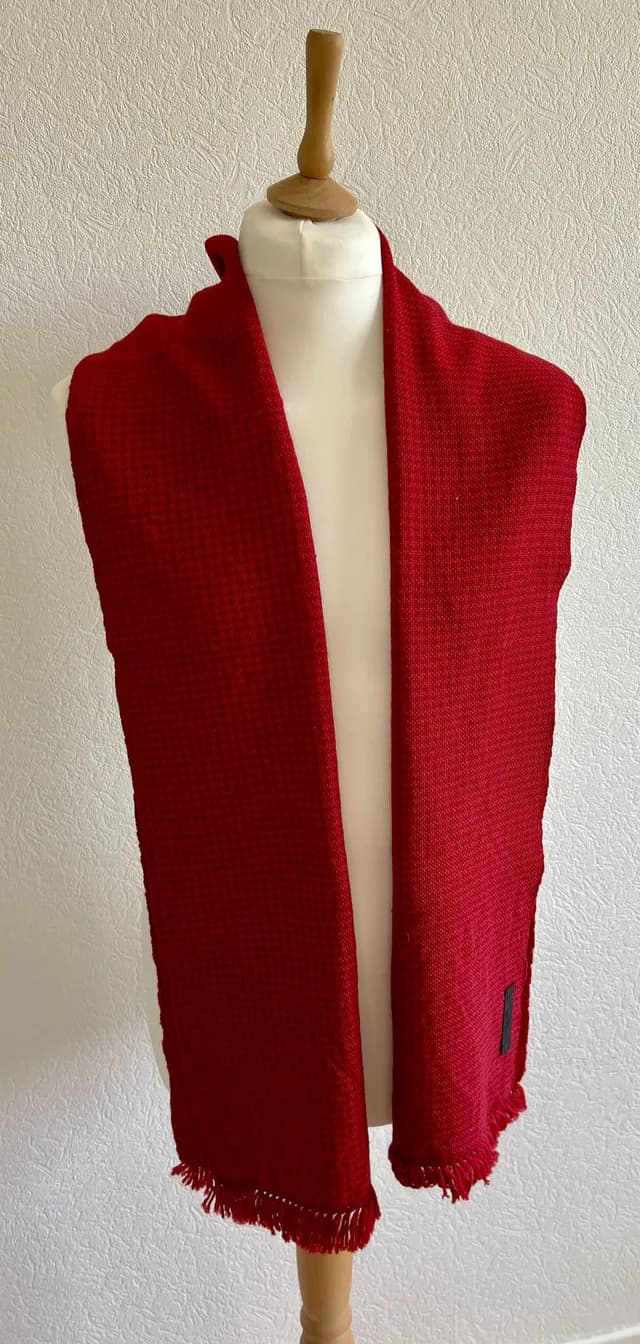Écharpe tissée rouge à franges présentée sur un buste de mannequin blanc