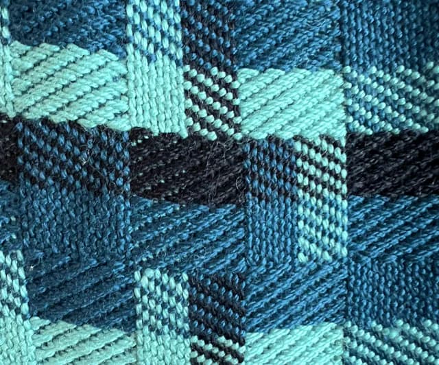 Gros plan sur le tissage artisanal géométrique en laine bleu canard, bleu et noir.