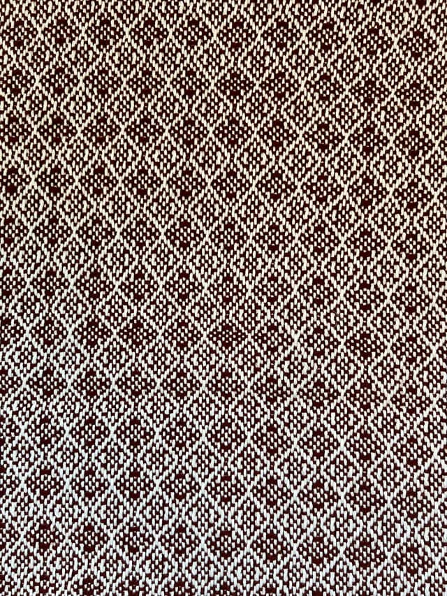 Détail du tissage artisanal à motif de losanges bordeaux et blancs de l'écharpe.
