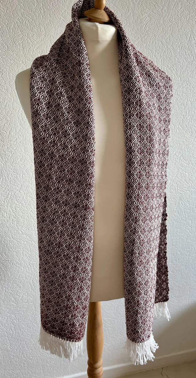 Écharpe bordeaux et écru à motif géométrique et franges, disposée sur un buste mannequin.