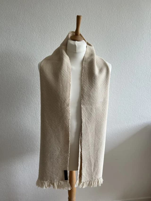 Écharpe tissée couleur champagne à franges nouées, drapée sur un buste de mannequin.
