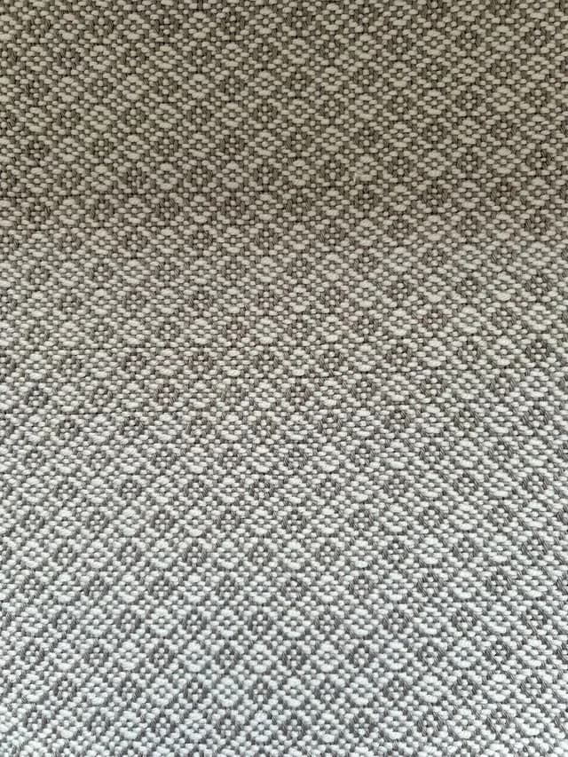 Gros plan sur le tissage artisanal serré et son motif géométrique en fils gris et écru.