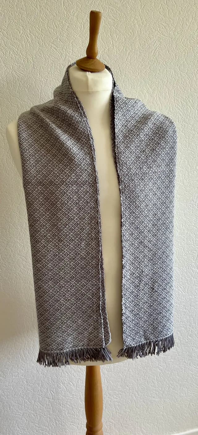 Écharpe tissée grise et blanche à motifs géométriques et franges, drapée sur un buste de mannequin.