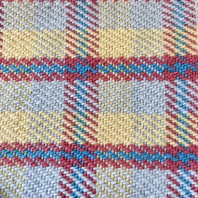 Gros plan sur le tissage sergé à carreaux tartan aux fils jaunes, bleus, rouges et blancs