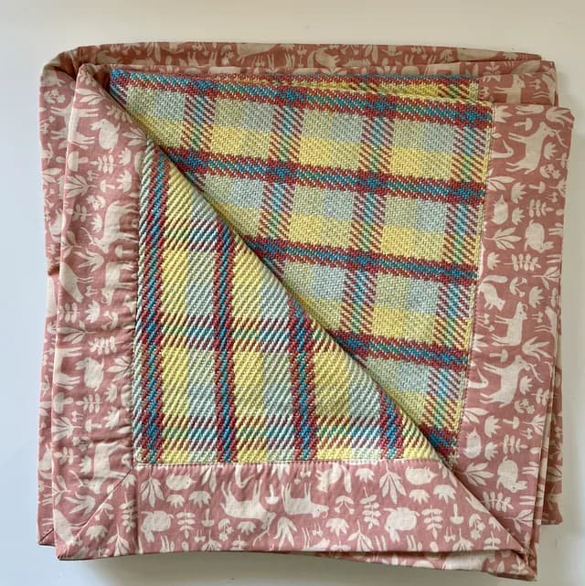 Plaid bébé plié à carreaux pastel bleu et jaune, bordé d'un tissu rose imprimé d'animaux