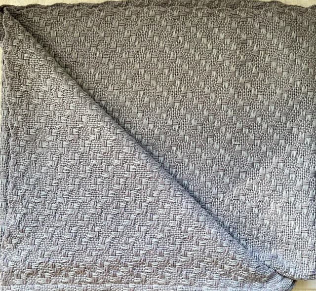 Plaid en coton tissé main gris avec motif texturé en relief, replié sur lui-même.