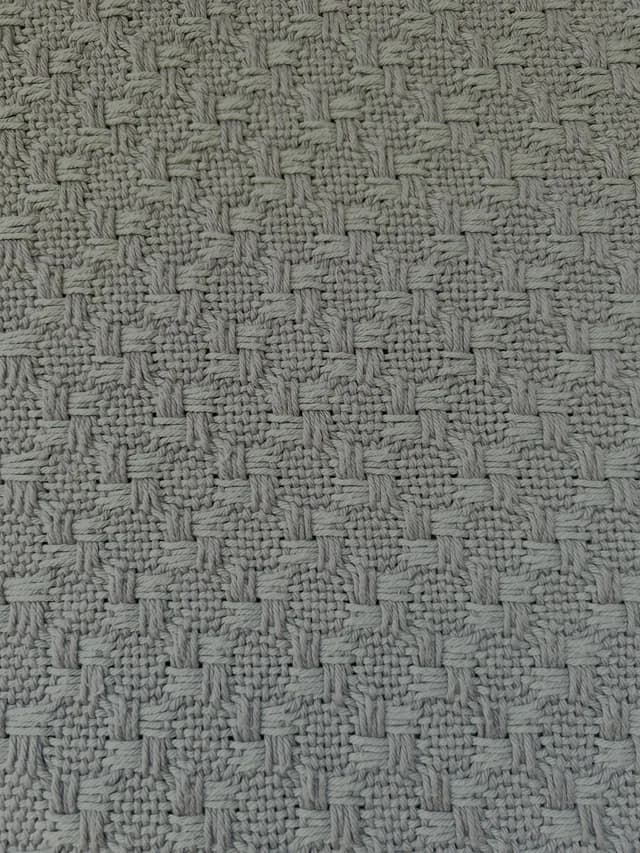 Gros plan sur le motif géométrique régulier du tissage de la couverture en coton gris.