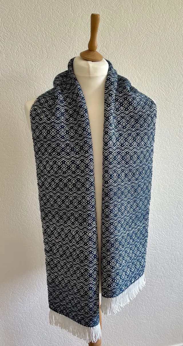 Écharpe tissée bleue et blanche à motifs géométriques et franges, drapée sur un mannequin.