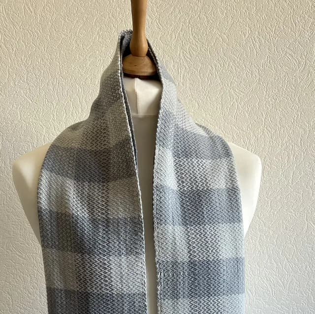 Écharpe tissée à carreaux blanc et gris drapée sur un mannequin de couture.