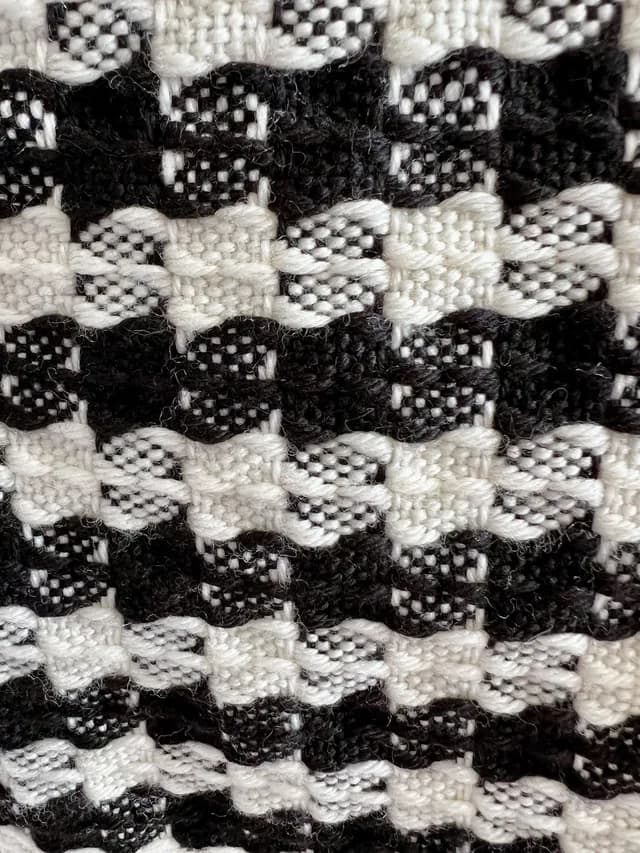 Gros plan sur le tissage texturé aux motifs géométriques noirs et blancs de l'écharpe en laine.