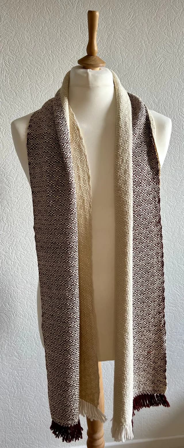 Écharpe bicolore bordeaux et beige à franges, drapée sur un mannequin de couture.