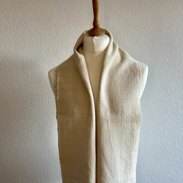 Écharpe tissée à motif chevron blanc et champagne drapée sur un buste de mannequin blanc.