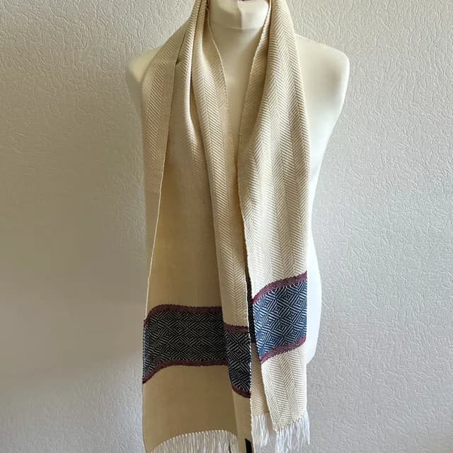 Écharpe tissée couleur champagne à chevrons avec bande bleue et rouge à motifs géométriques et franges.
