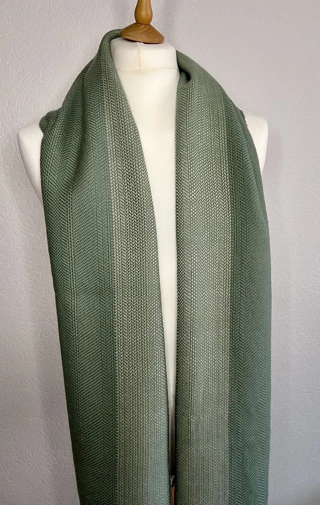 Écharpe tissée aux nuances vert sauge drapée sur un mannequin de couture.
