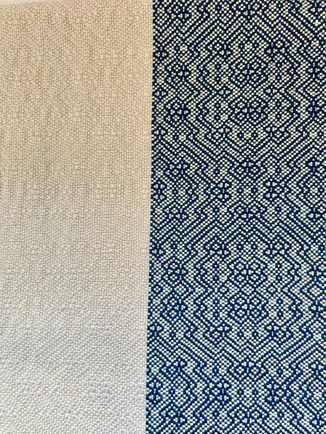 Gros plan sur le tissage d'une écharpe, montrant une partie unie beige écru et des motifs bleus détaillés.