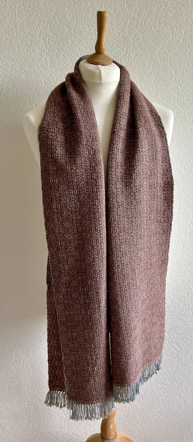 Écharpe tissée rose chiné avec franges claires, présentée sur un mannequin de couture.