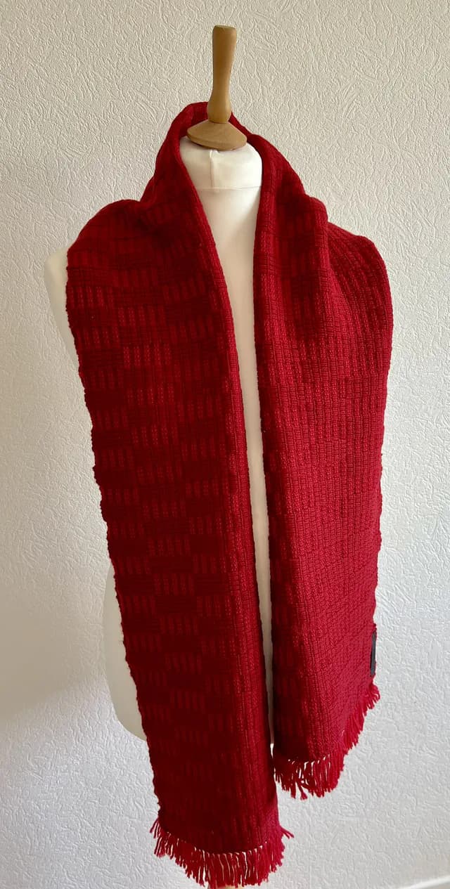 Écharpe rouge à franges portée sur un buste de mannequin blanc.