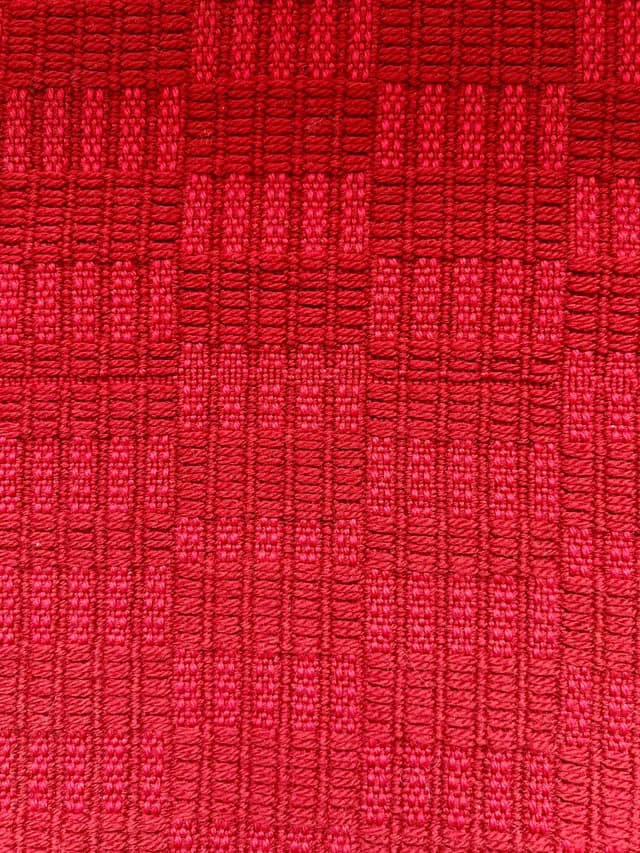 Gros plan sur le tissage texturé aux motifs géométriques de l'écharpe rouge.
