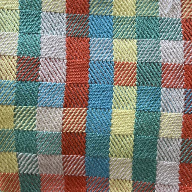 Détail du tissage artisanal aux carrés texturés multicolores bleu, vert, jaune et terracotta.