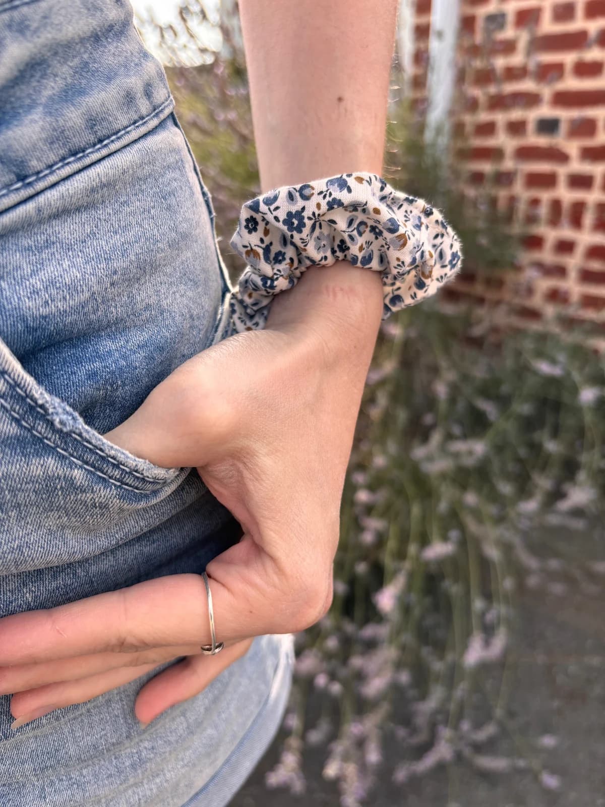 Chouchou à motif floral bleu porté au poignet, main dans la poche d'un jean.