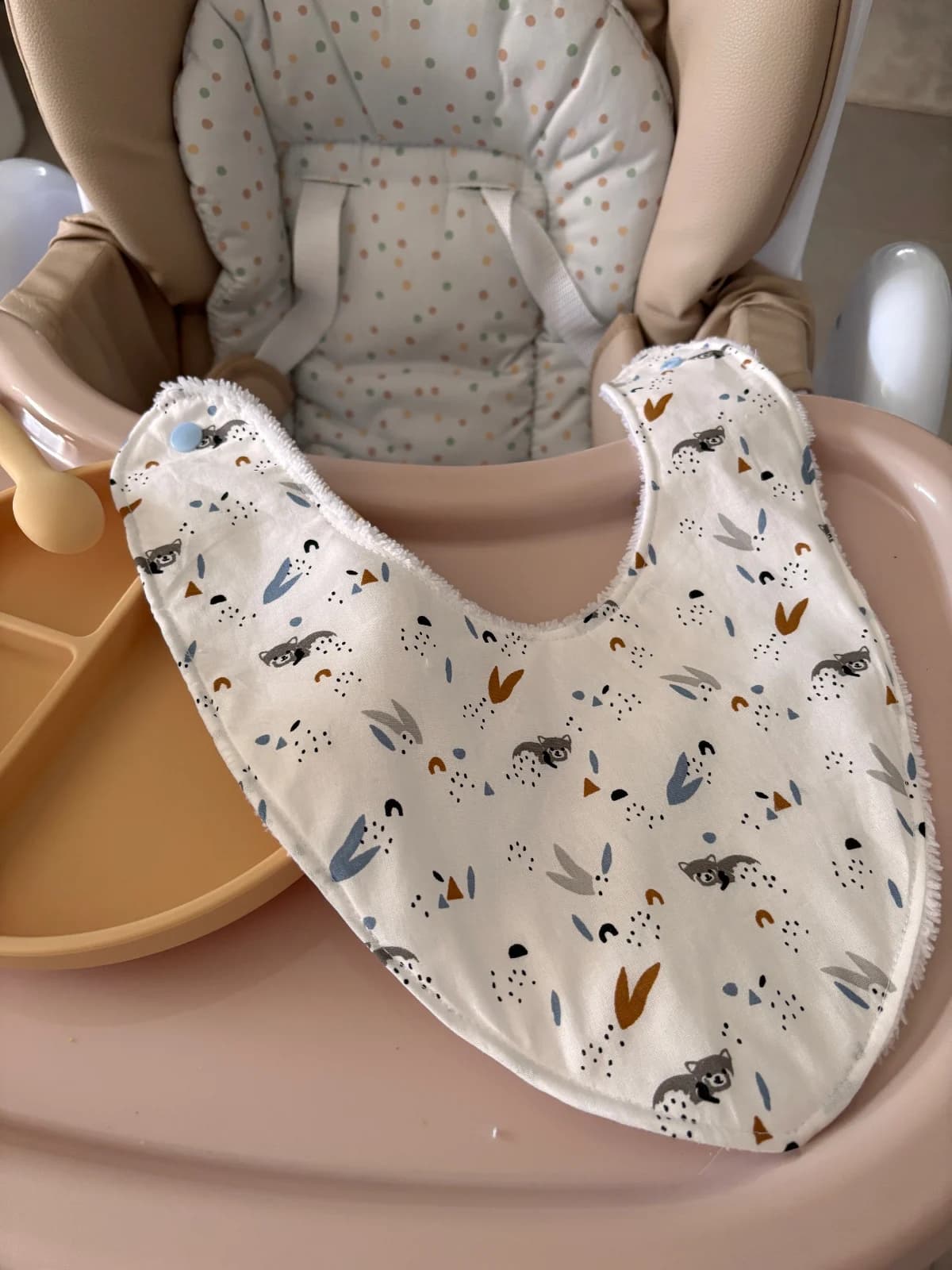 Bavoir bandana à motifs animaux étalé à plat avec bouton pression bleu sur tablette de chaise haute