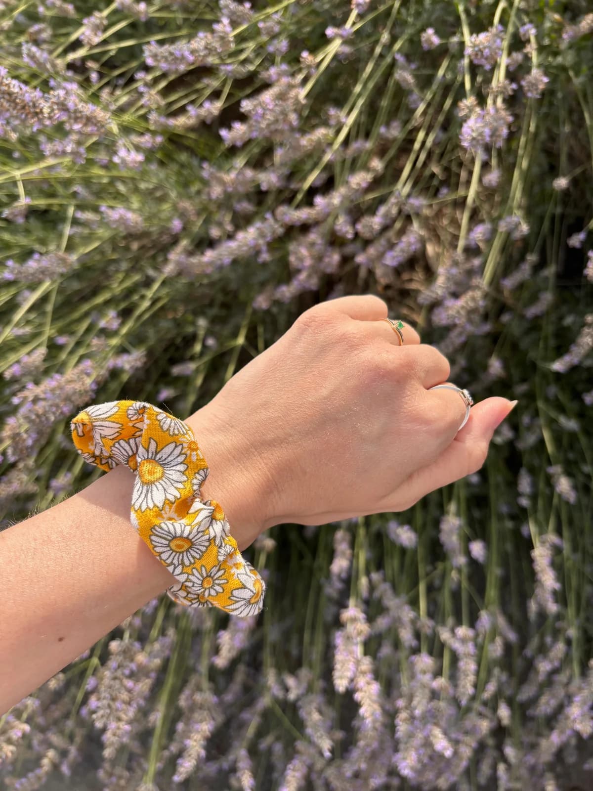 Chouchou fleuri jaune et blanc porté au poignet devant des branches de lavande.