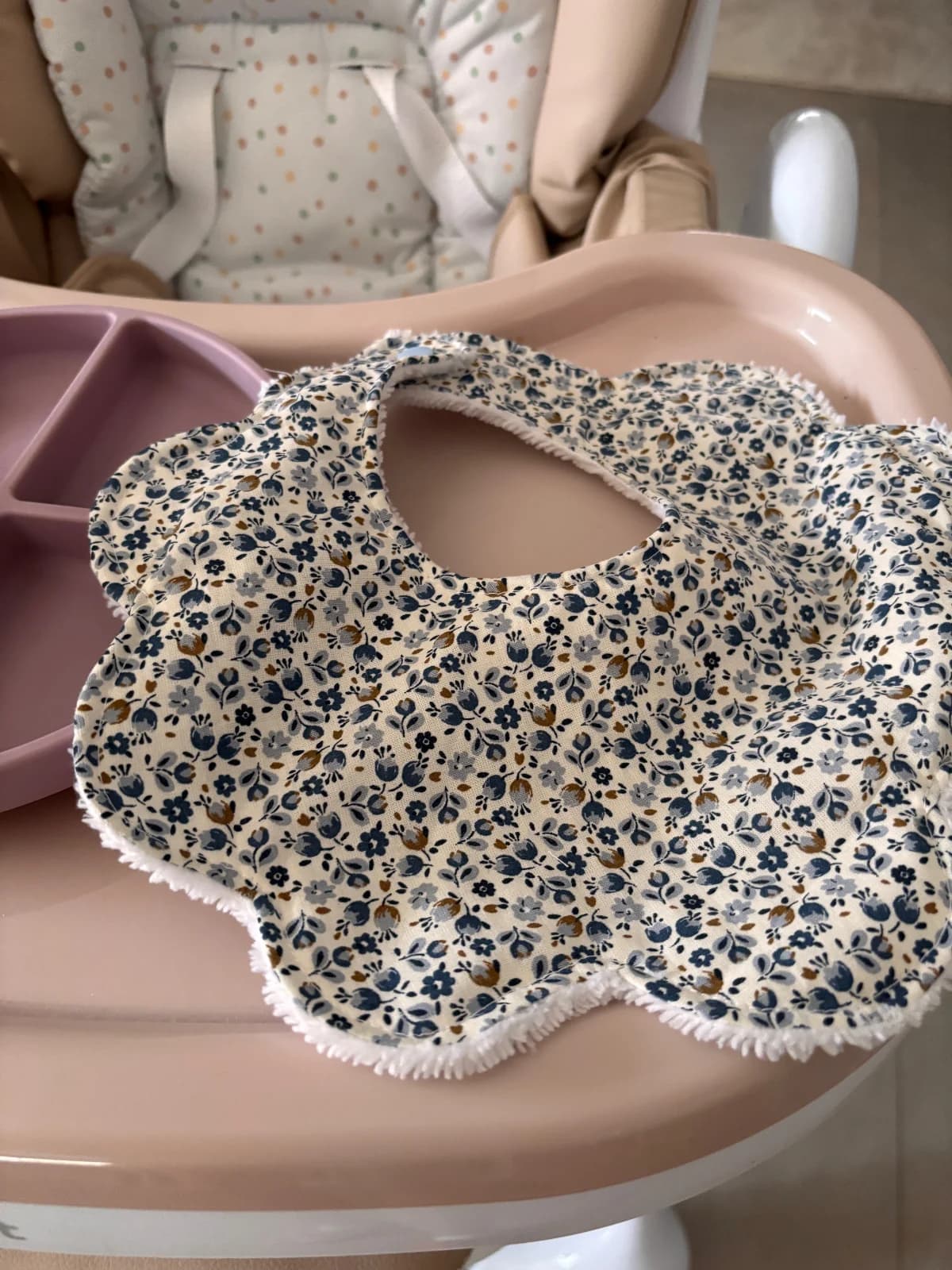 Bavoir festonné fleuri avec bouton-pression posé sur le plateau d'une chaise haute.