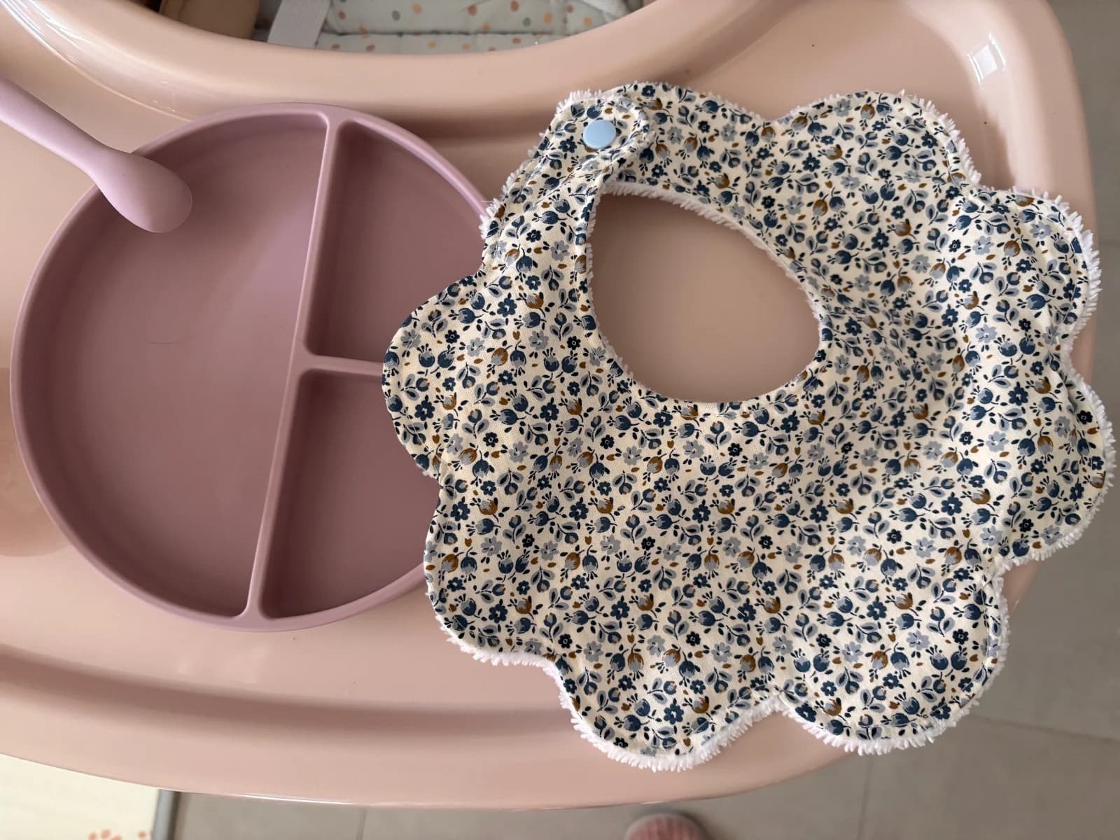 Bavoir en forme de fleur à imprimé fleuri posé à côté d'une assiette rose pour bébé.