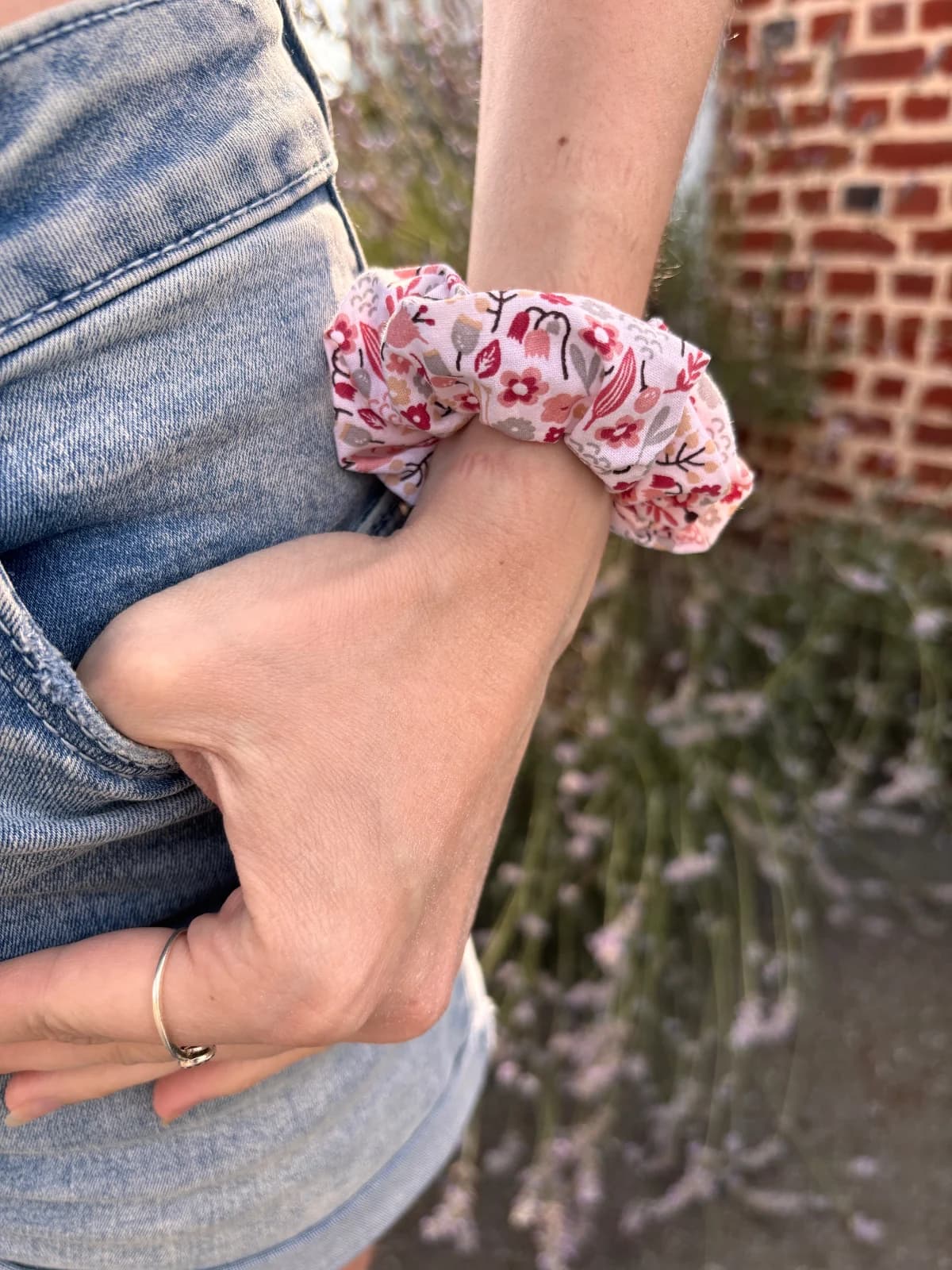Chouchou en tissu à motifs floraux roses et rouges porté au poignet avec un jean