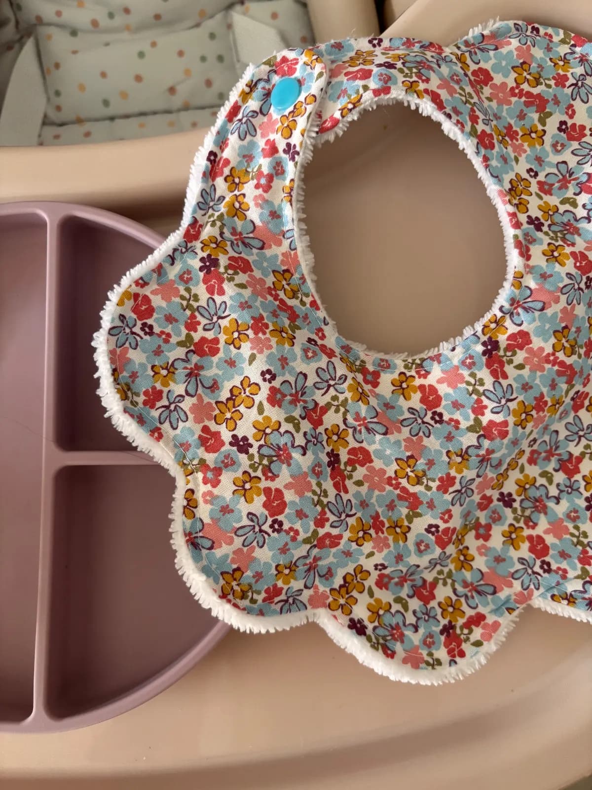 Vue rapprochée du bavoir fleuri forme pétale avec bouton-pression turquoise