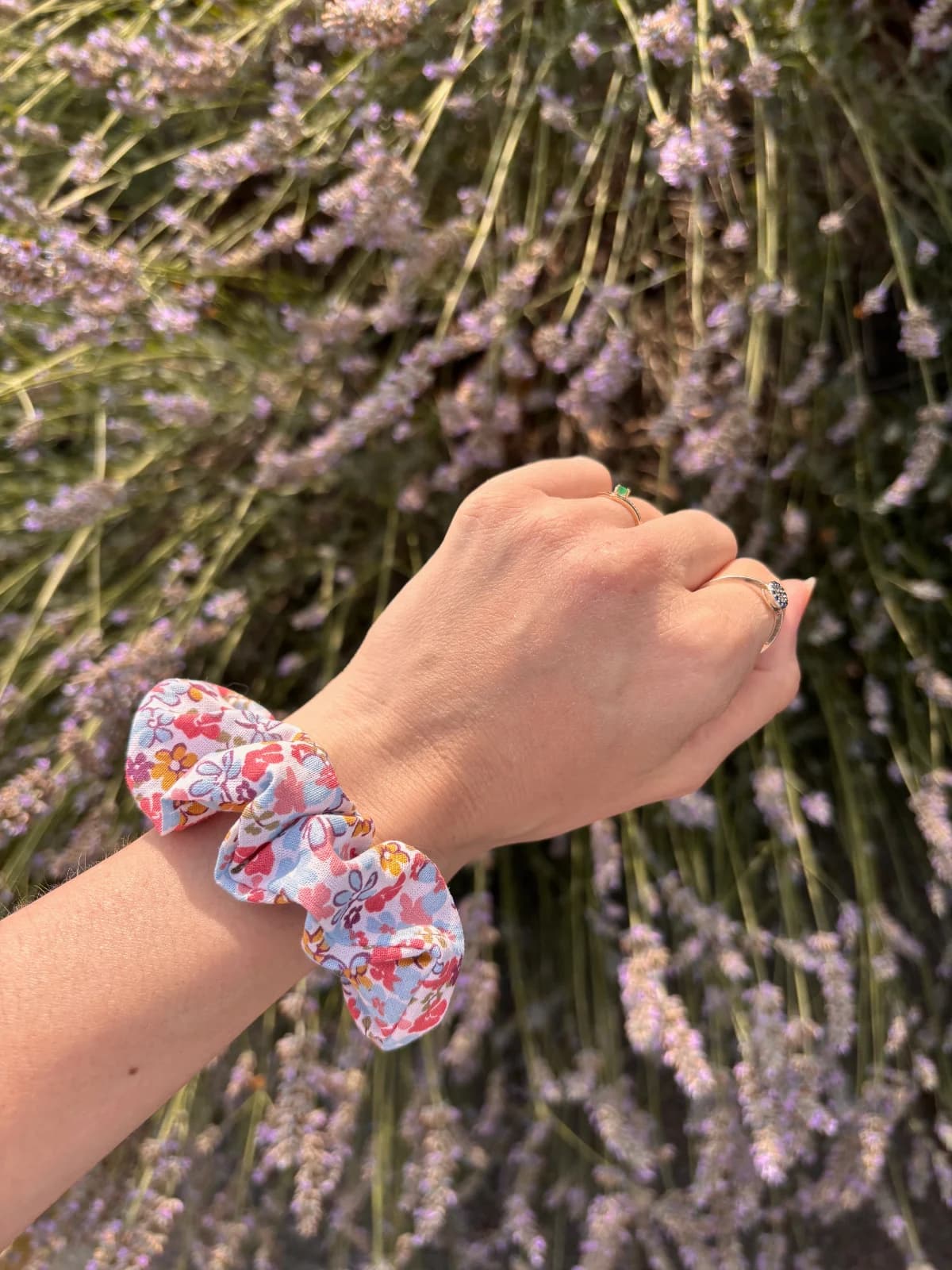 Chouchou fleuri rose et bleu au poignet d'une main devant un massif de fleurs