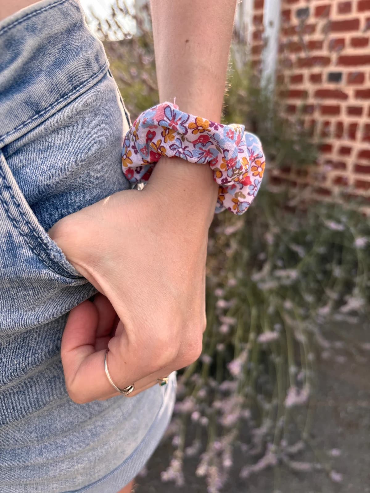 Chouchou en tissu à motifs floraux colorés porté au poignet sur fond de jean