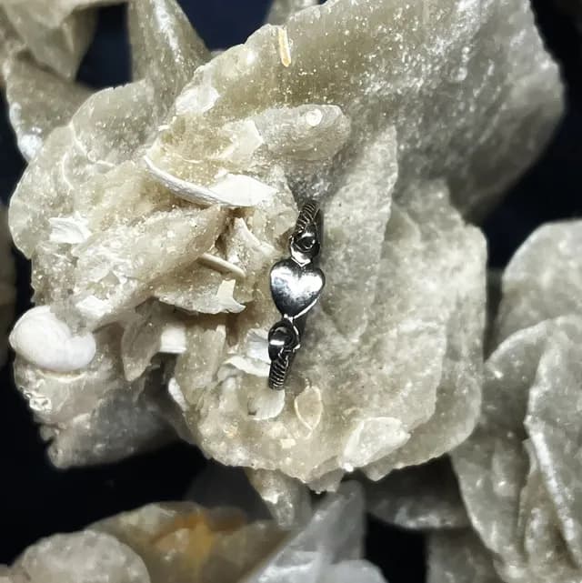 Bague fine en argent ornée d'un motif cœur posée sur une roche minérale claire